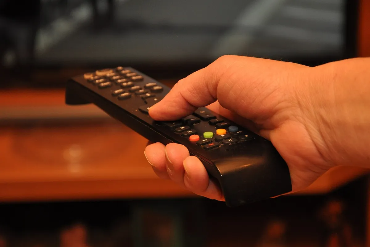 Hand med fjärrkontroll riktad mot tv:n