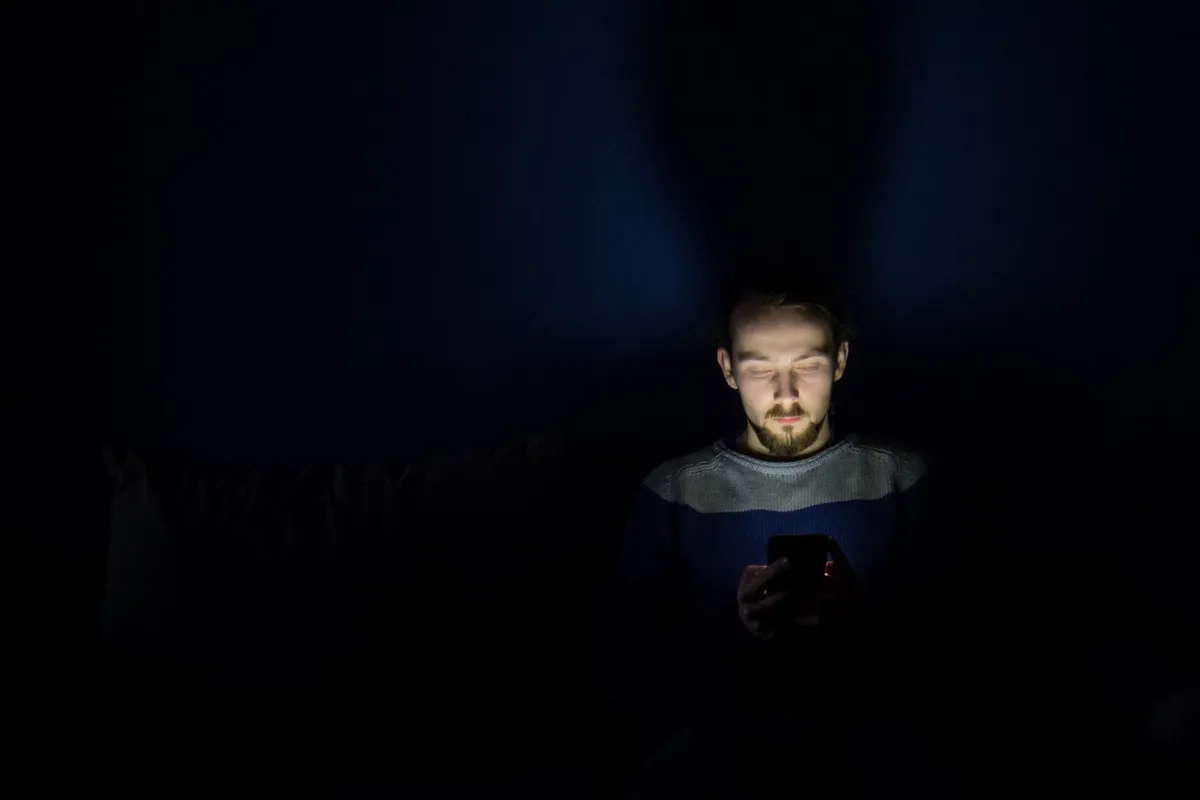 Man som tittar i mobilen i mörkret