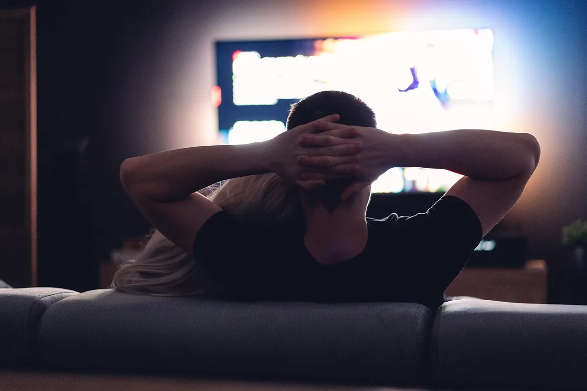 Person som lutar sig bakåt framför en upplyst tv